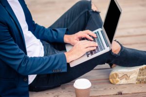 closeup-hombre-mano-trabajando-puente-madera-laptop-cafe-notebook_109800-3928